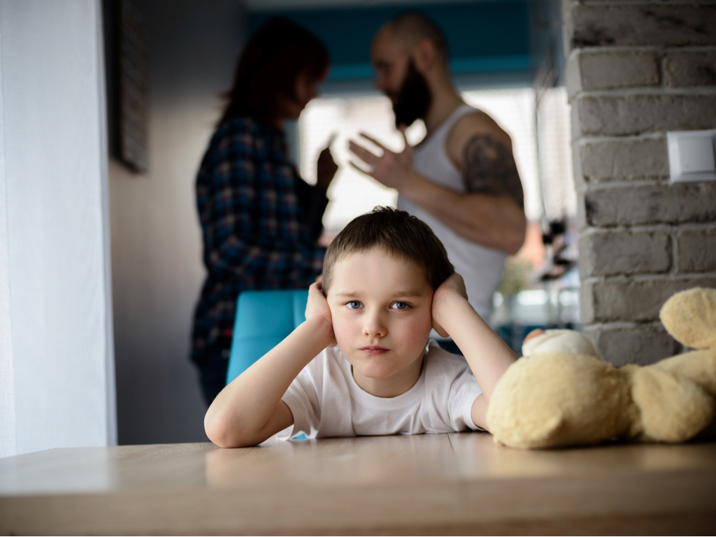 child holding hands against ears as parents fight in the background - Parental Alienation