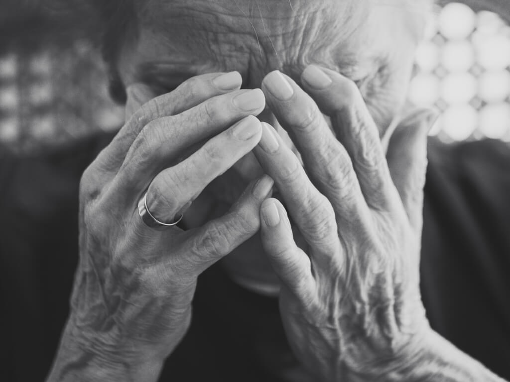 elderly woman holding hands to face